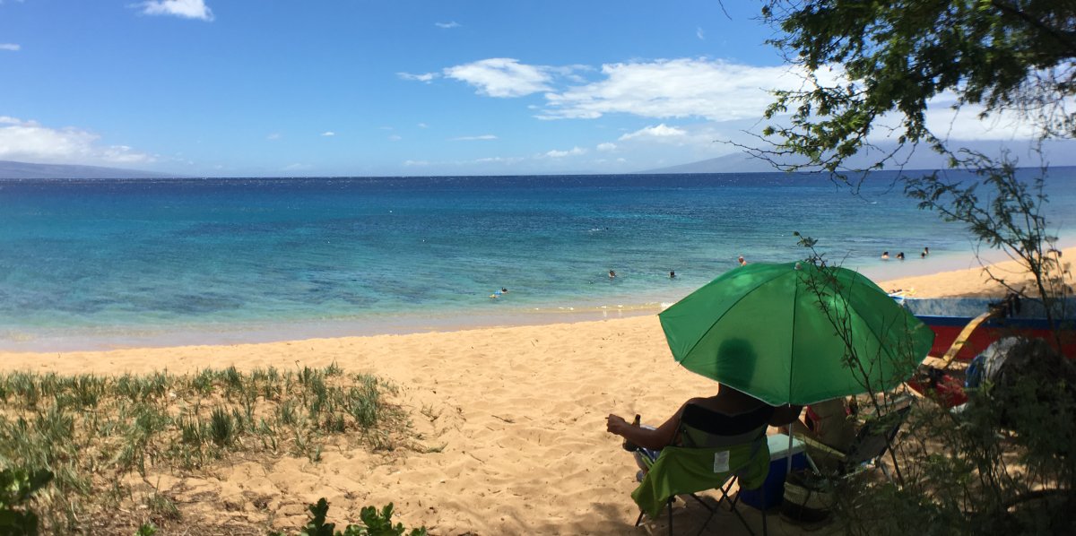 View of a couple sitting on Kaanapali Beach with snorkelers in the water