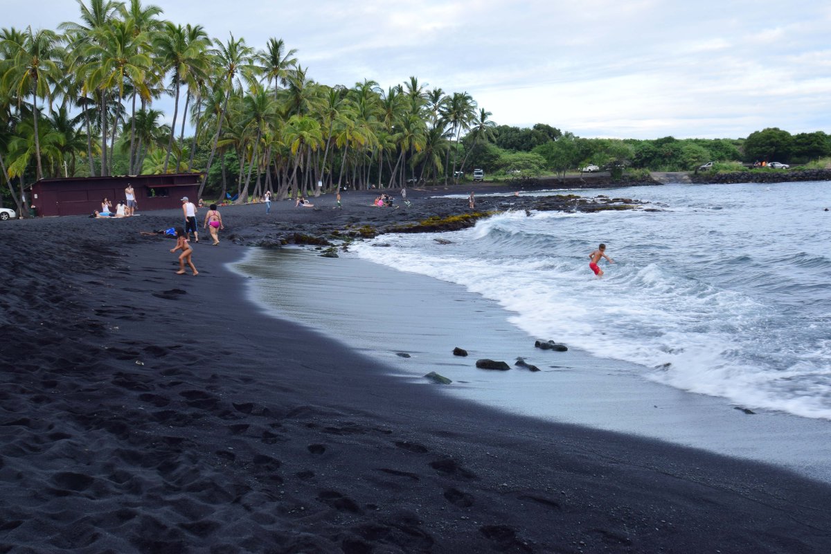 People enjoying the waves on the black sand of Punaluu Beach on the Big Island of Hawaii