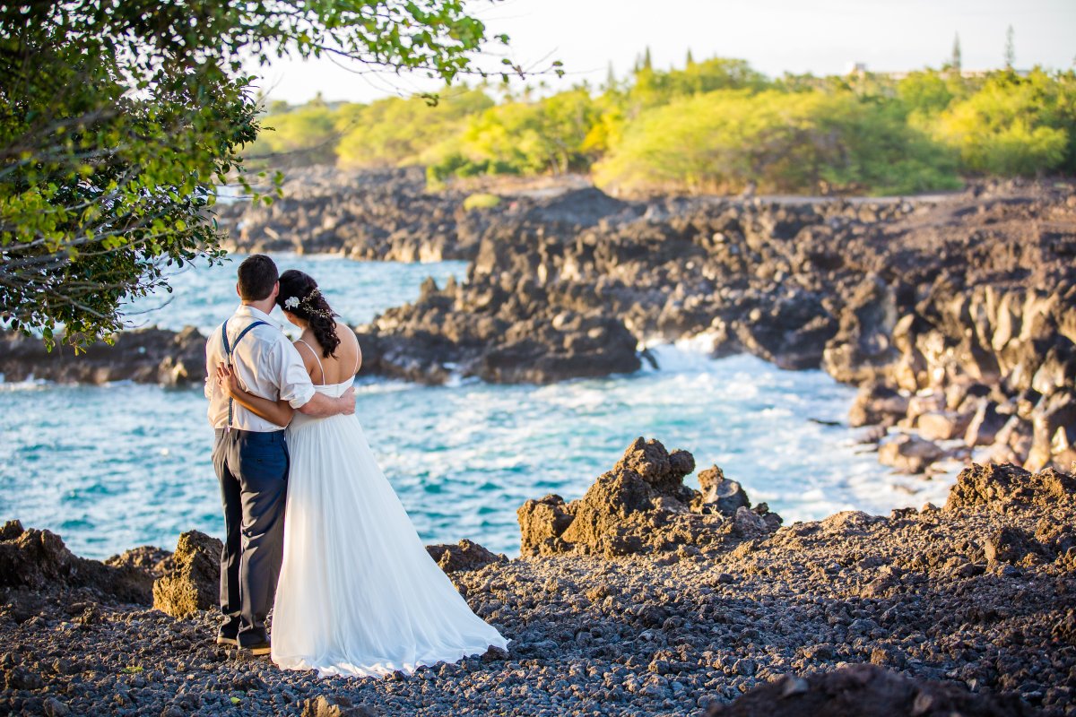 View of bride and groom on shore of Hawaiian lava rock beach on wedding day
