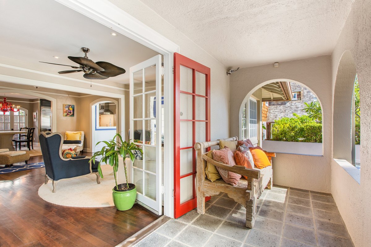 Hale Mahie's covered front porch with a wooden bench seat and a ceiling fan. Behind the bench is a view of the living room and kitchen counter.