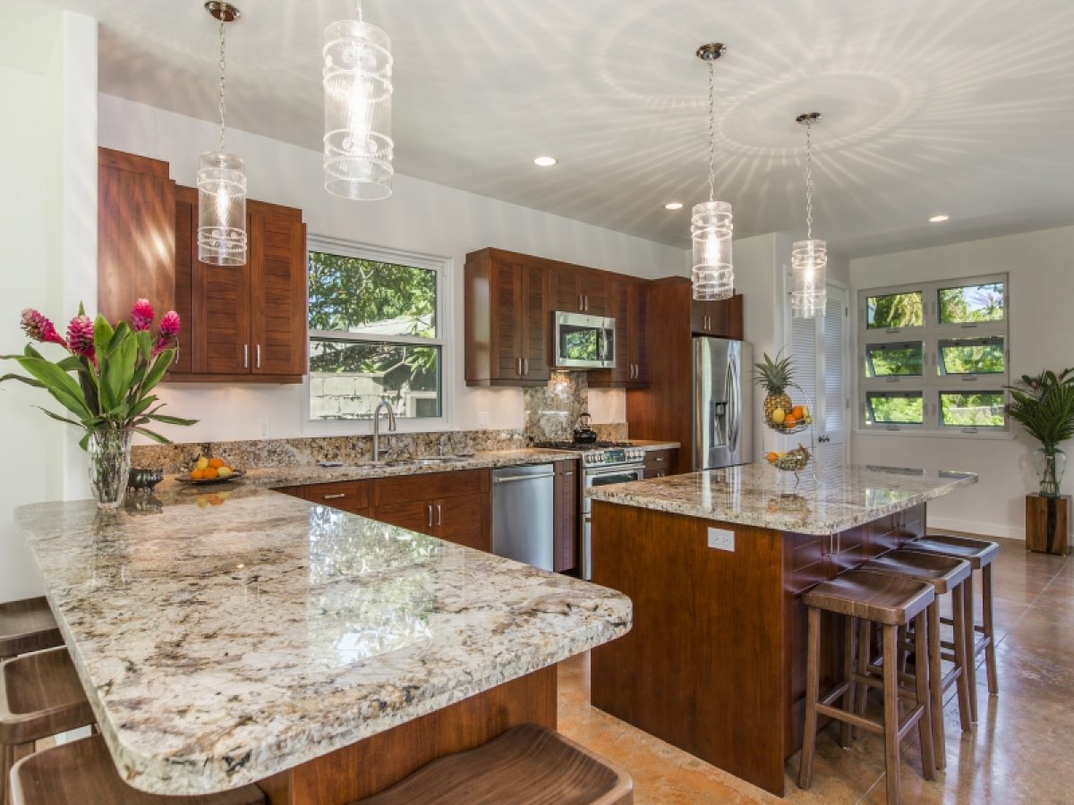 Hale Nani Lanikai's kitchen features a spacious and open layout with dark wood cabinets, granite counters, and a large kitchen island with seating