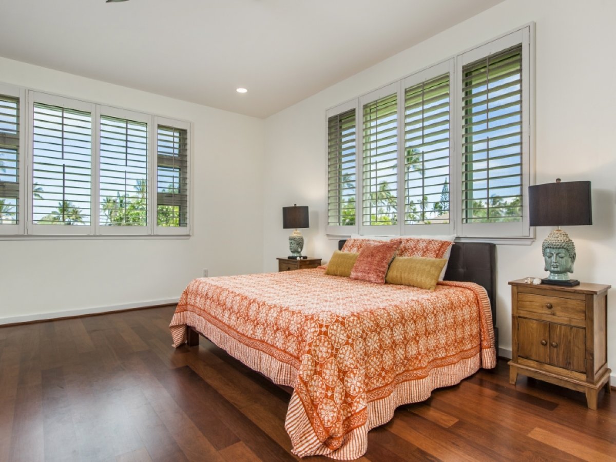 Primary bedroom with king-size bed and large windows with white plantation shutters that allow ample natural light to filter in