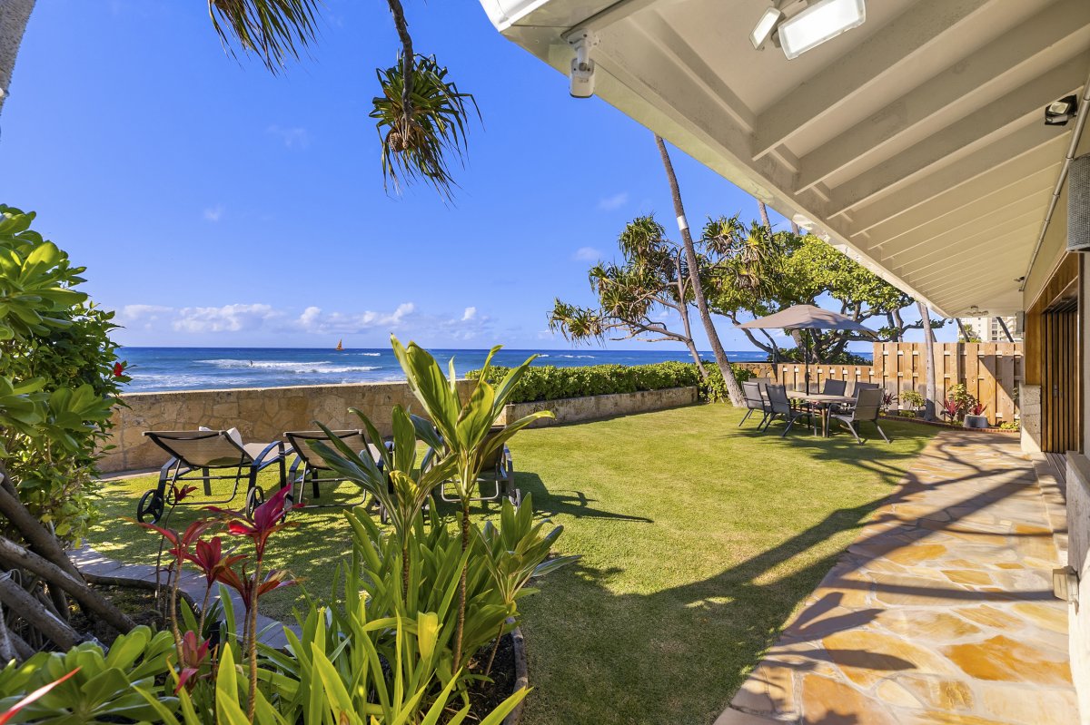 Hale Makai's oceanside grassy lawn complete with comfortable lounge chairs, outdoor seating and a shaded umbrella