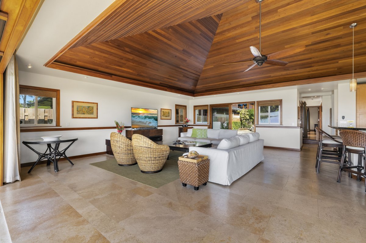 Spacious living room area with a wooden ceiling, flat-screen TV, ceiling fan and a door that opens up to Hale Makai's pool