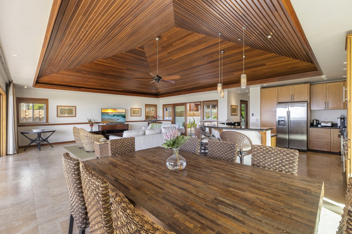 A large dining table that comfortably seats 8 people and next to it is the living room and kitchen area in Hale Makai at Diamond Head