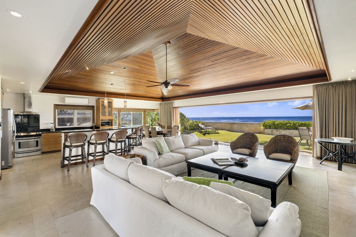 Step into the vaulted living room space at Hale Makai and be greeted by a lush grassy lawn surrounded by vibrant greenery, offering breathtaking ocean views