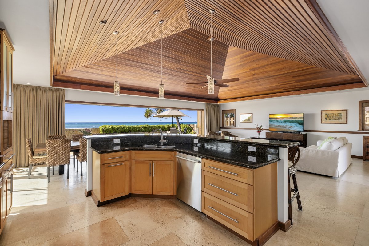 Hale Makai's kitchen features a breakfast bar with a stunning ocean view, complemented by elegant light-colored pendant lamps hanging from the ceiling