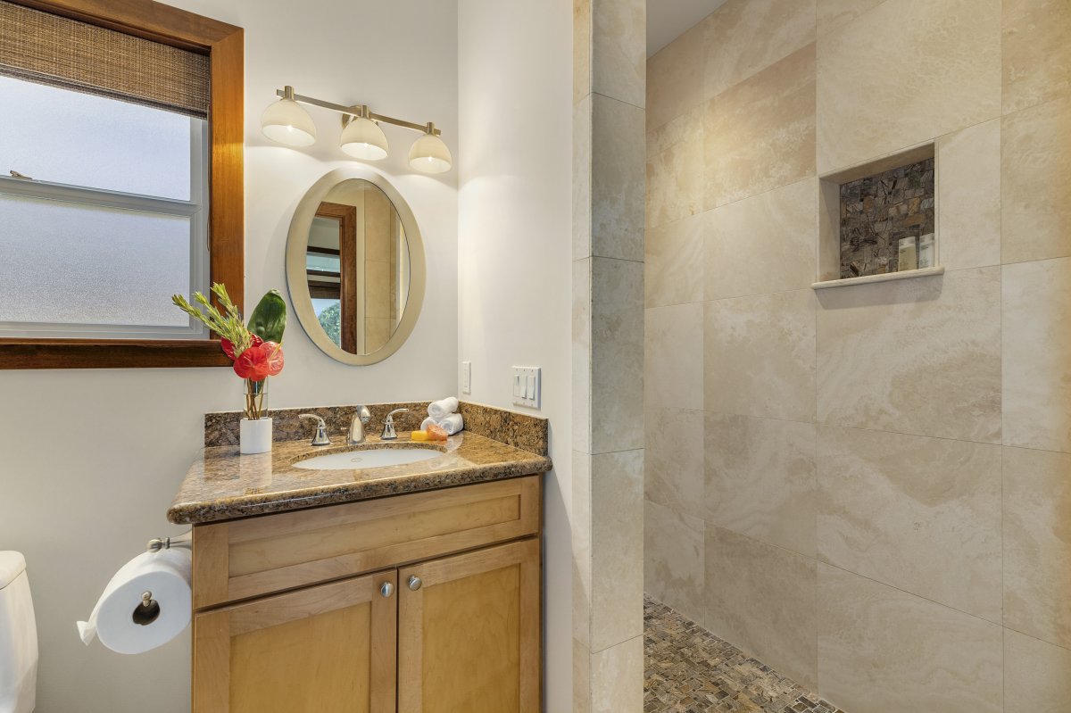 Hale Makai's luxurious Third Bedroom En-suite with a marble countertop, a mirror above the sink, a cabinet with drawers and shelves and toilet