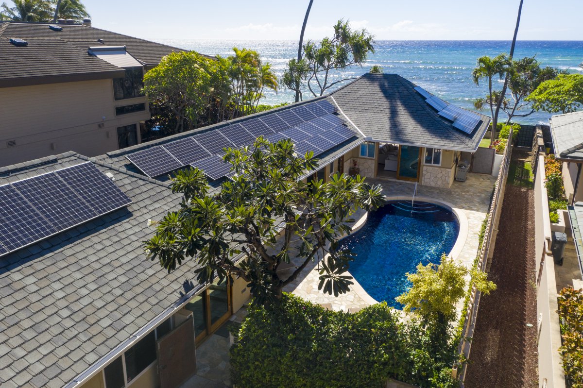 Overhead view of Hale Makai at Diamond Head vacation home featuring lush green surroundings, a sparkling pool, solar panels atop the roof, and majestic ocean views