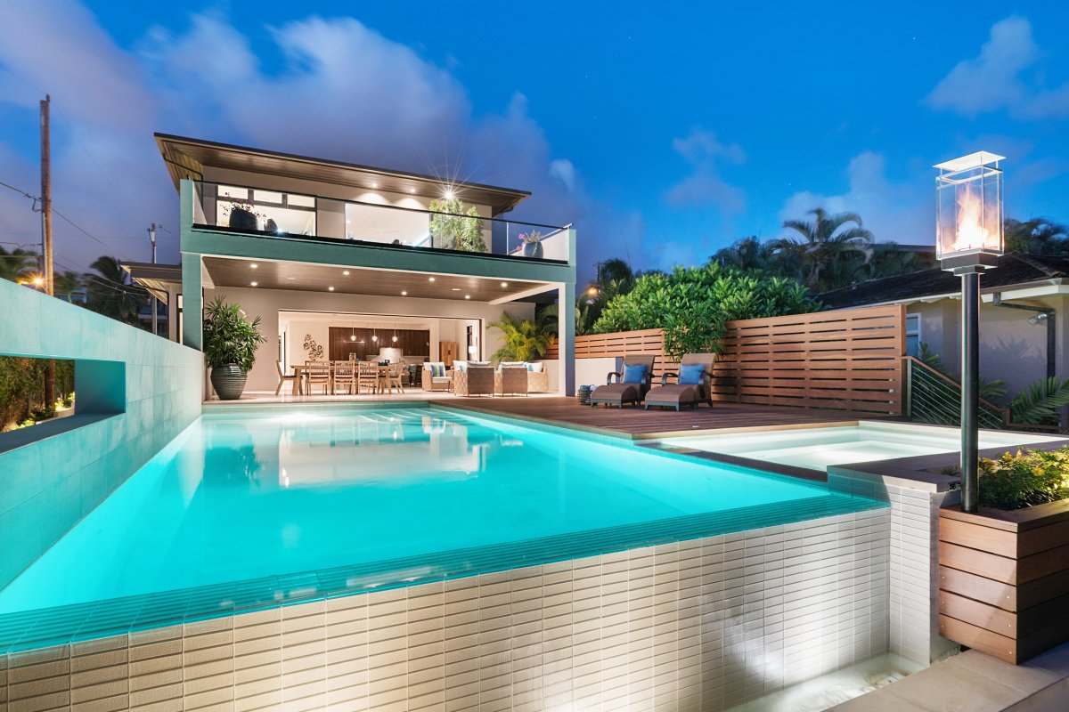 Evening view of Diamond Head Grandeur Villa on Oahu with swimming pool, covered lanai, patio chairs, table, and lounge chair next to the pool