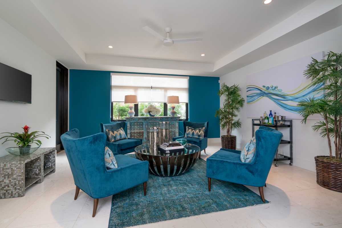 The seating area features four plush, teal-colored armchairs, a ceiling fan, and a flat-screen TV