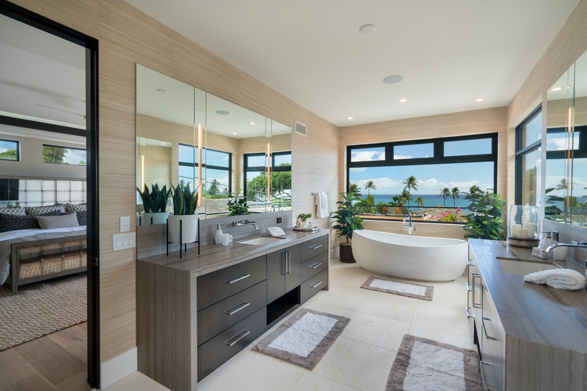 Modern bathroom with large vanities, storage, countertops, large framed mirrors, tiled flooring, and bathtub positioned viewing the ocean