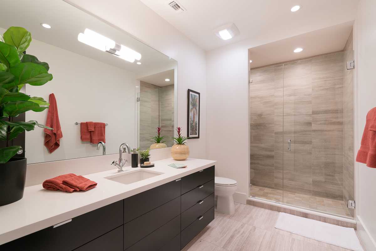 Stylish bathroom with large single-sink vanity,  countertop, drawers, mirror, toilet, and glass-doored walk-in shower