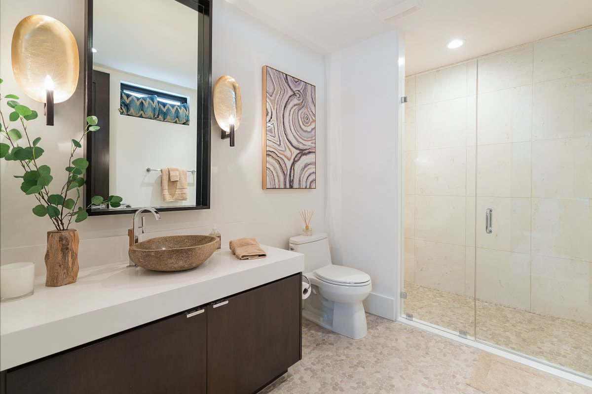 Modern bathroom with single-sink vanity, countertop, drawers, large frameless mirror, toilet, and walk-in shower with a glass partition