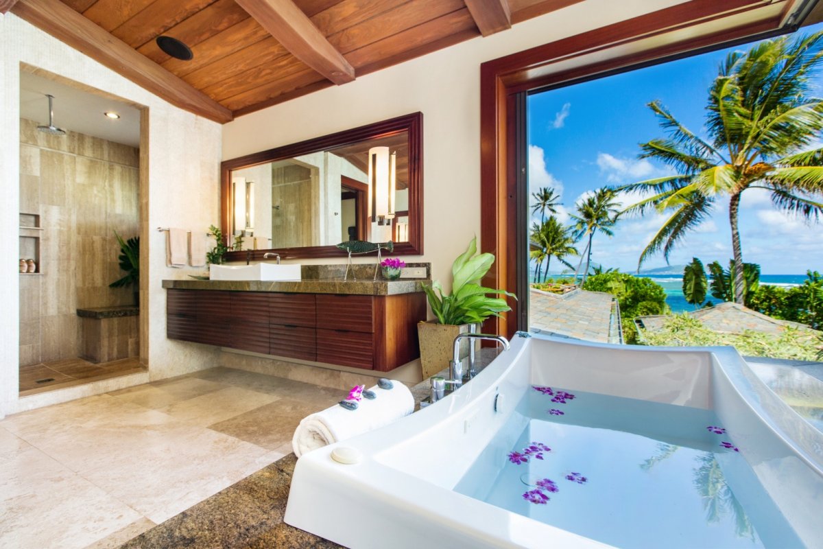 Luxurious primary bathroom with a bathtub facing the ocean view, walk-in shower, and vanity