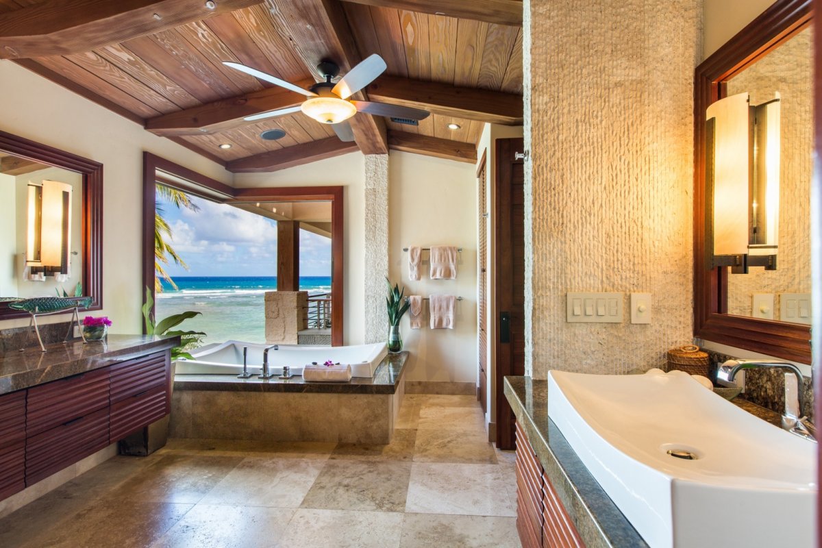 Luxurious primary bathroom with a bathtub facing the ocean, vanity, and white ceramic sink. Above the sink is a mirror