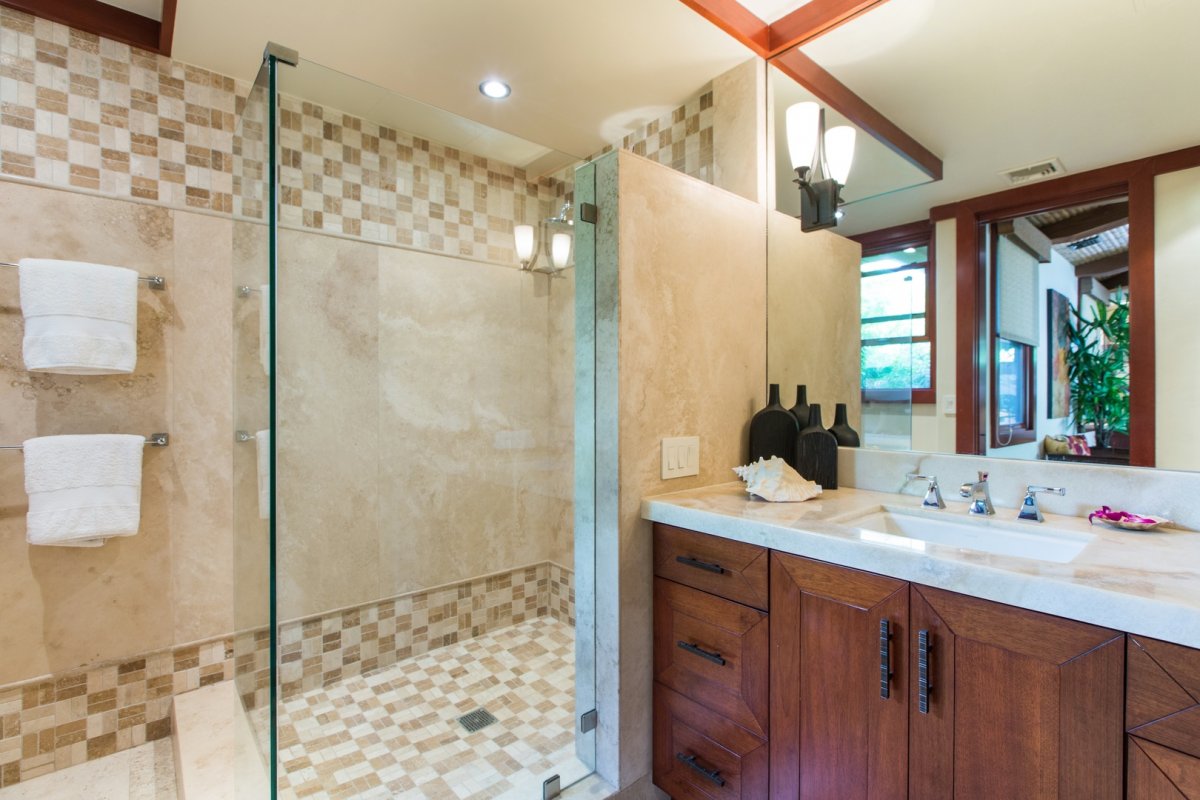 Banyan House bathroom with a glass door walk-in shower, large mirror, and a single sink on a marble countertop