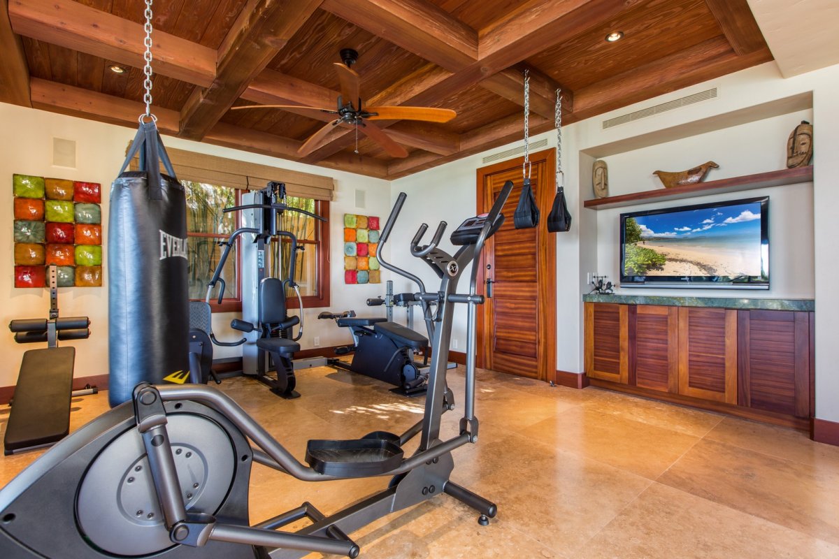 Banyan House gym room with multi-purpose weight machine, heavy bag, elliptical machine, ceiling fan and flat-screen TV