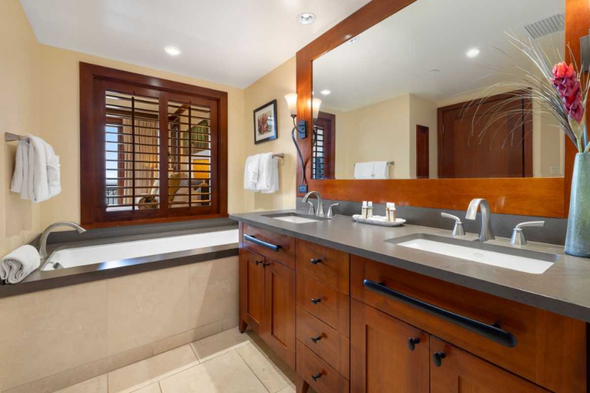 Elegant ensuite bathroom with a large mirror, dual sinks, and a bathtub, featuring wooden accents and natural lighting.