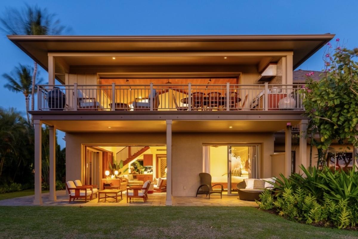 Back of this spacious home at twilight, showcasing upper and lower decks and grassy lawn.