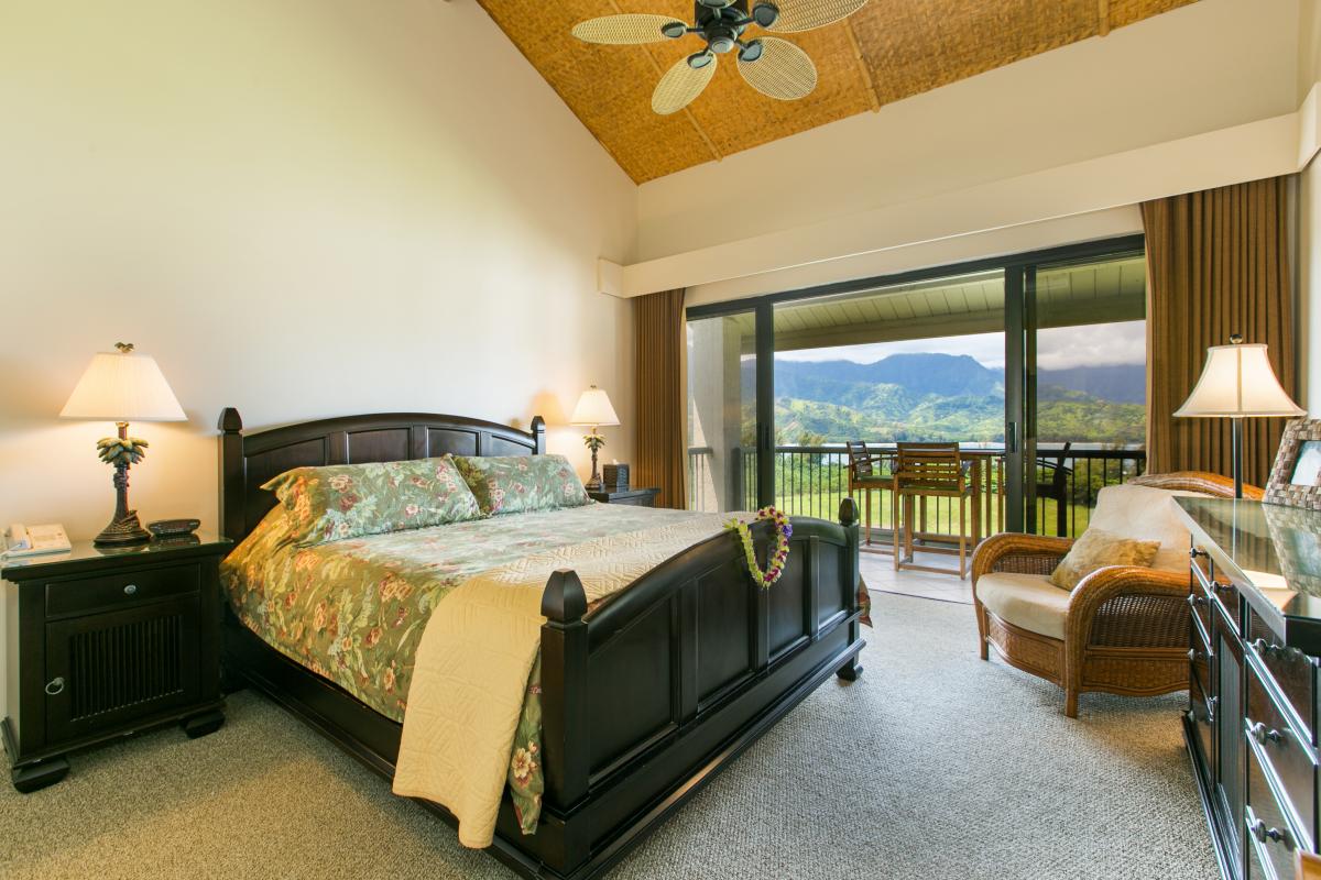 Spacious bedroom with a king-sized bed, elegant furnishings, and access to a private lanai offering breathtaking mountain views.