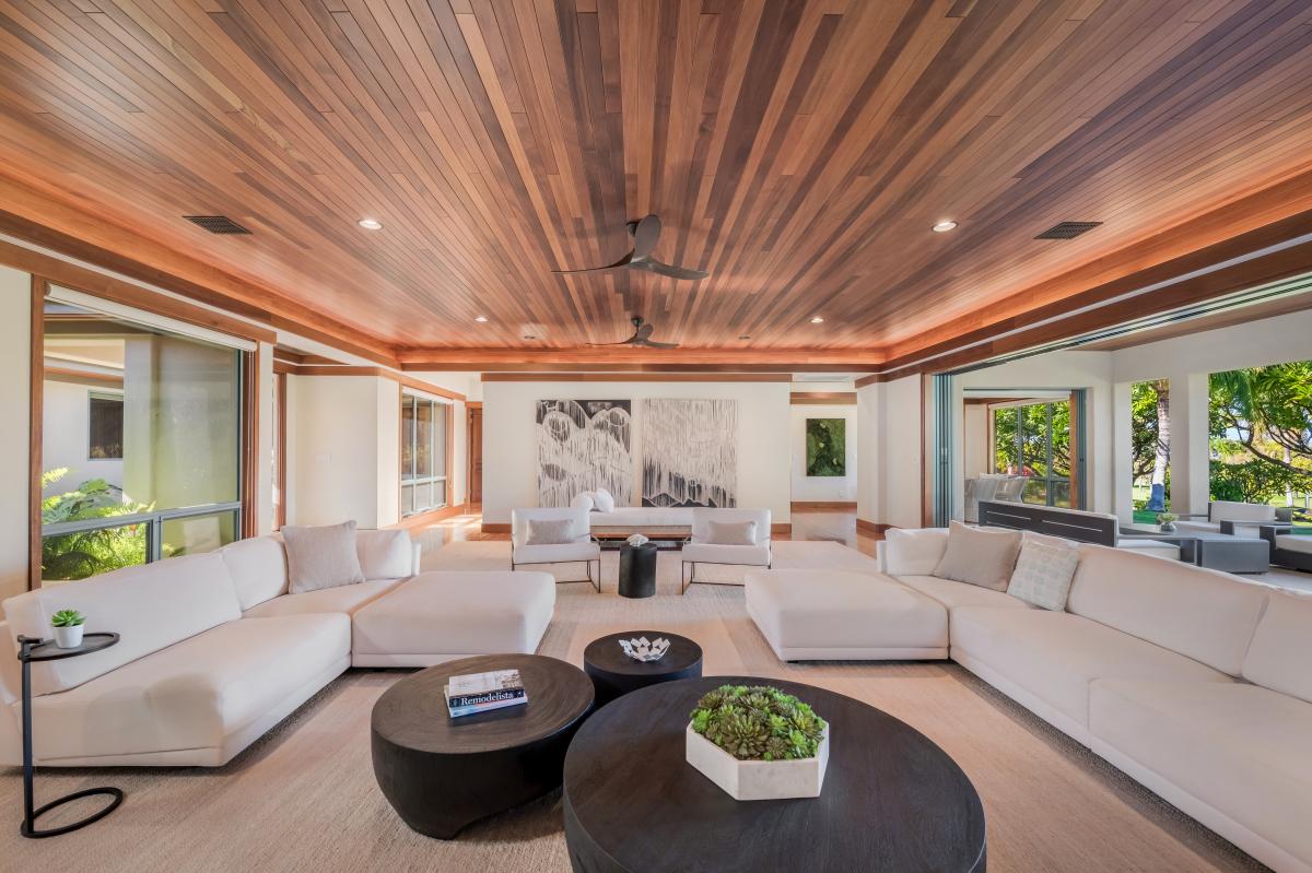 Spacious living room with luxurious seating, featuring a stunning wood-paneled ceiling and views of the lush outdoors.