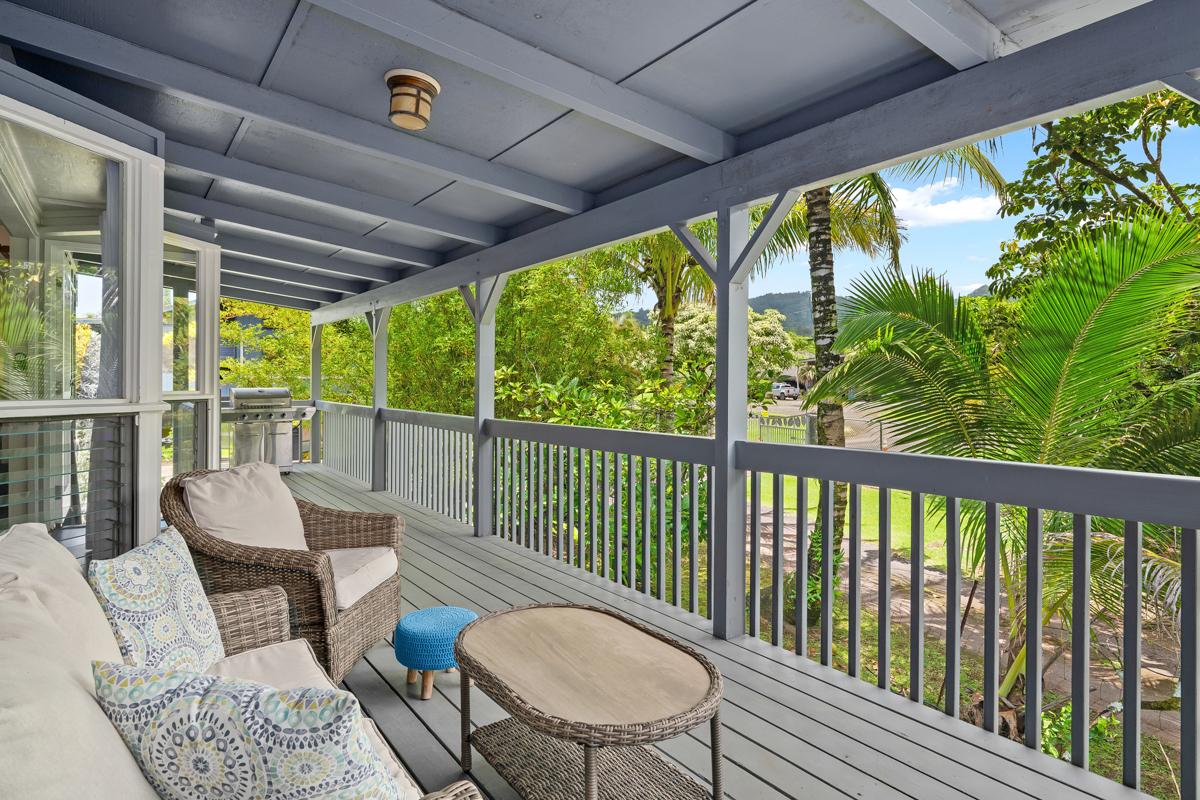 Two chairs and a small table on the lanai, framed by the garden beyond the railing.