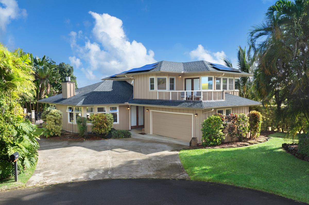 Modern two-story tropical home with solar panels, landscaped gardens, and palm trees in a peaceful residential setting.