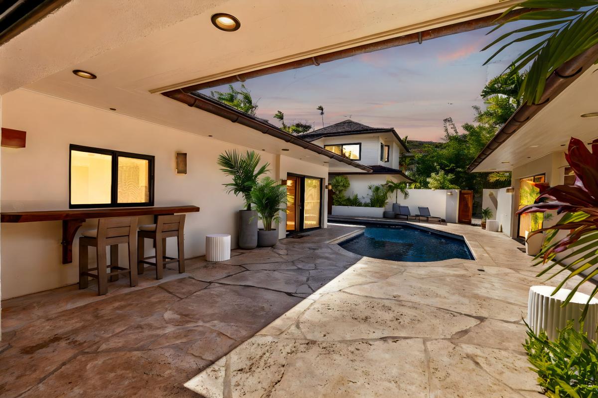 Enjoy sunset cocktails at the poolside bar, complete with built-in seating and lush garden surroundings for a resort-style experience at home.
