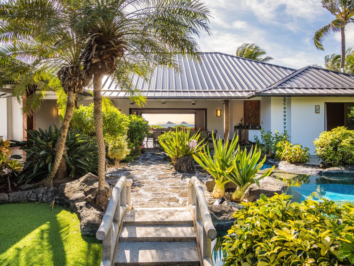 Signature tropical entryway framed by palm trees, flowers, and flowing water.