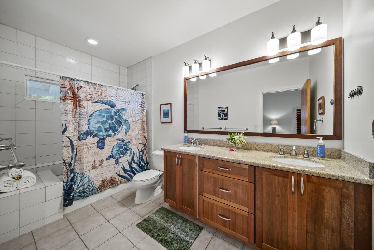 Ensuite bath featuring dual sinks, granite counters, and a shower/tub combo accented by local art for a touch of island charm.