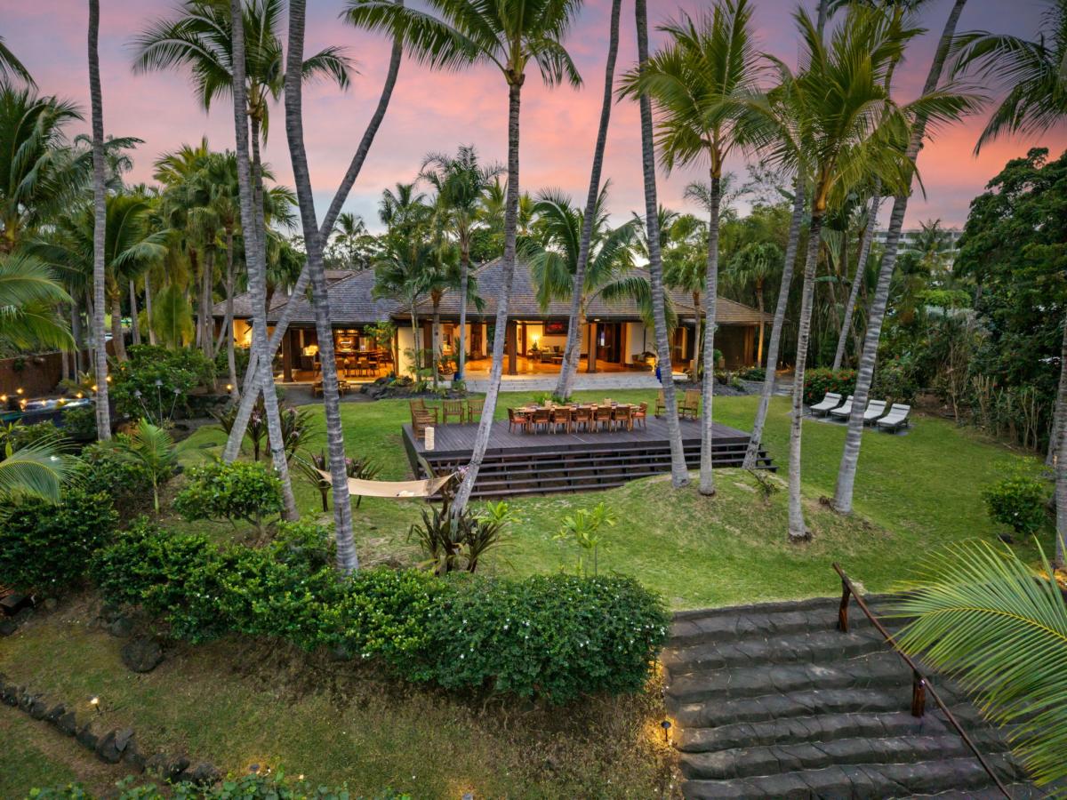 Tropical villa surrounded by swaying palms under a vibrant sunset sky, featuring spacious grounds and outdoor entertaining areas.