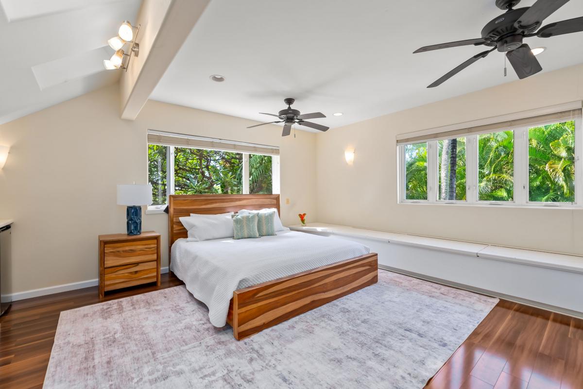 Wake up to lush tropical views through panoramic windows in your spacious bedroom, where warm wood tones and ceiling fans create perfect comfort.
