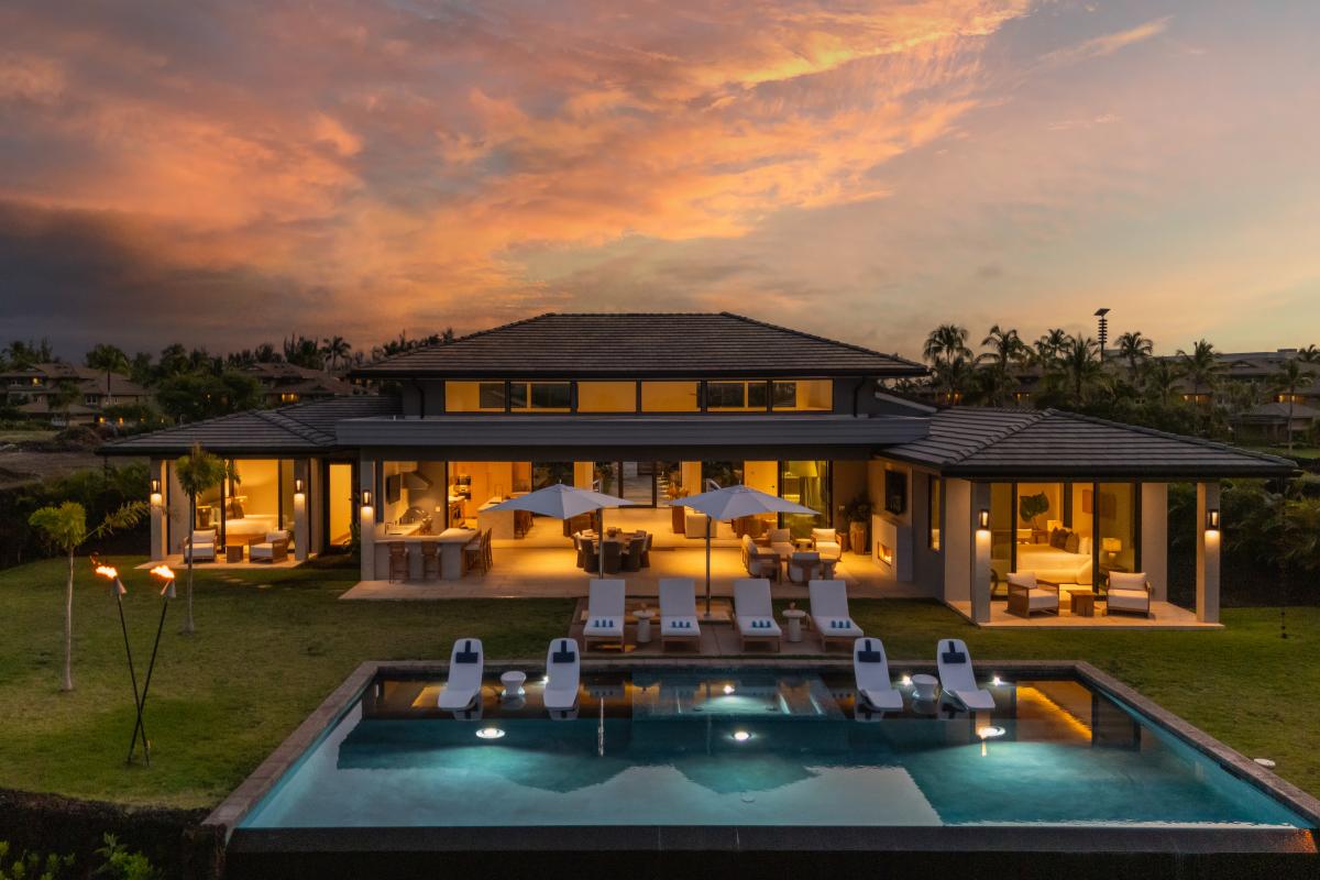 Luxurious villa surrounded by tropical palms, featuring a stunning swimming pool and outdoor dining areas under dramatic sunset skies.