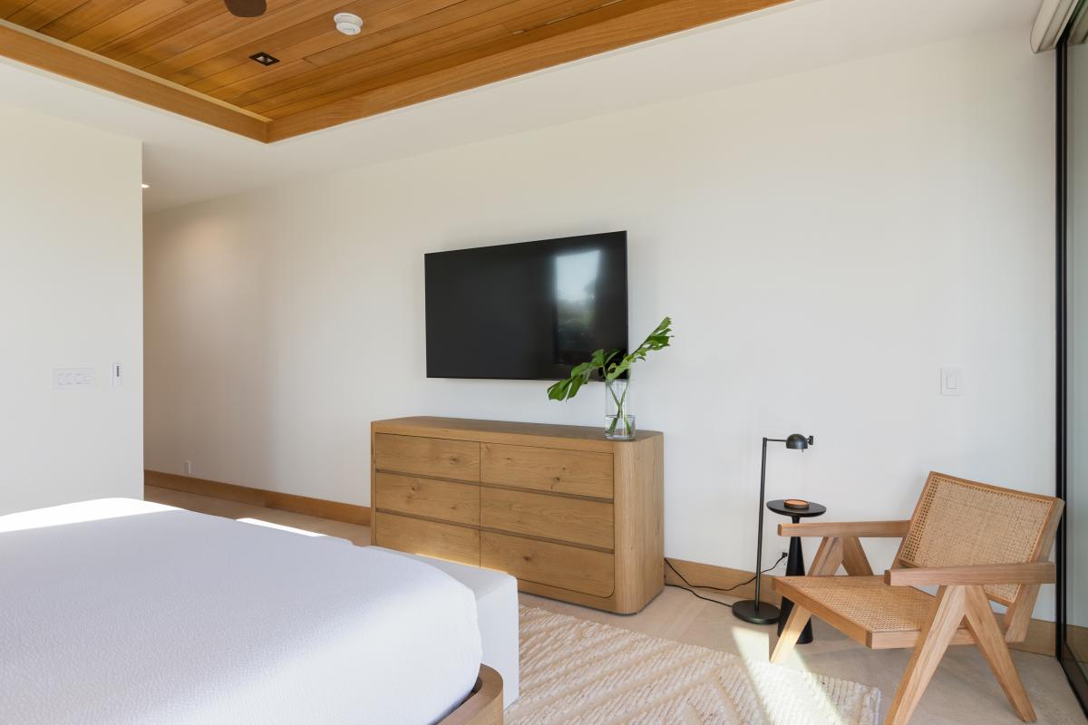 Unwind in your serene bedroom featuring warm wood tones, a wall-mounted TV, and stylish furniture for the perfect retreat.