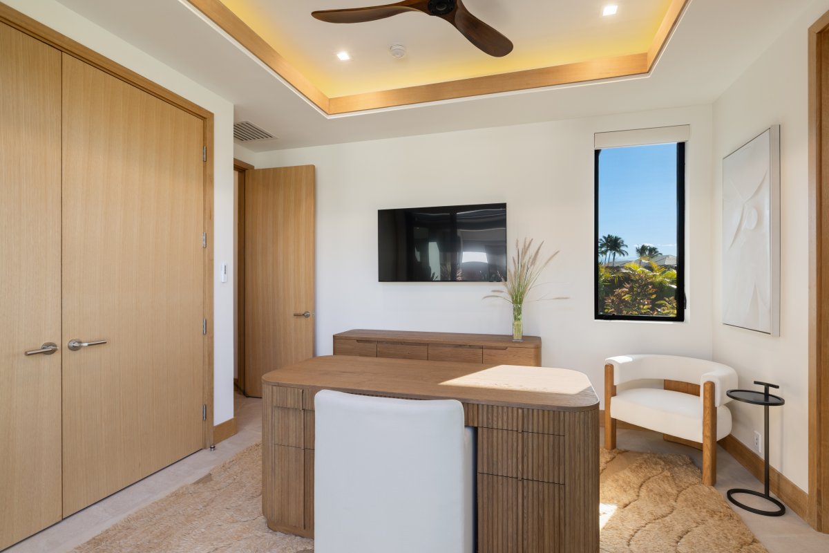 Your private workspace features warm wood accents and a wall-mounted TV, with tropical views through your window.