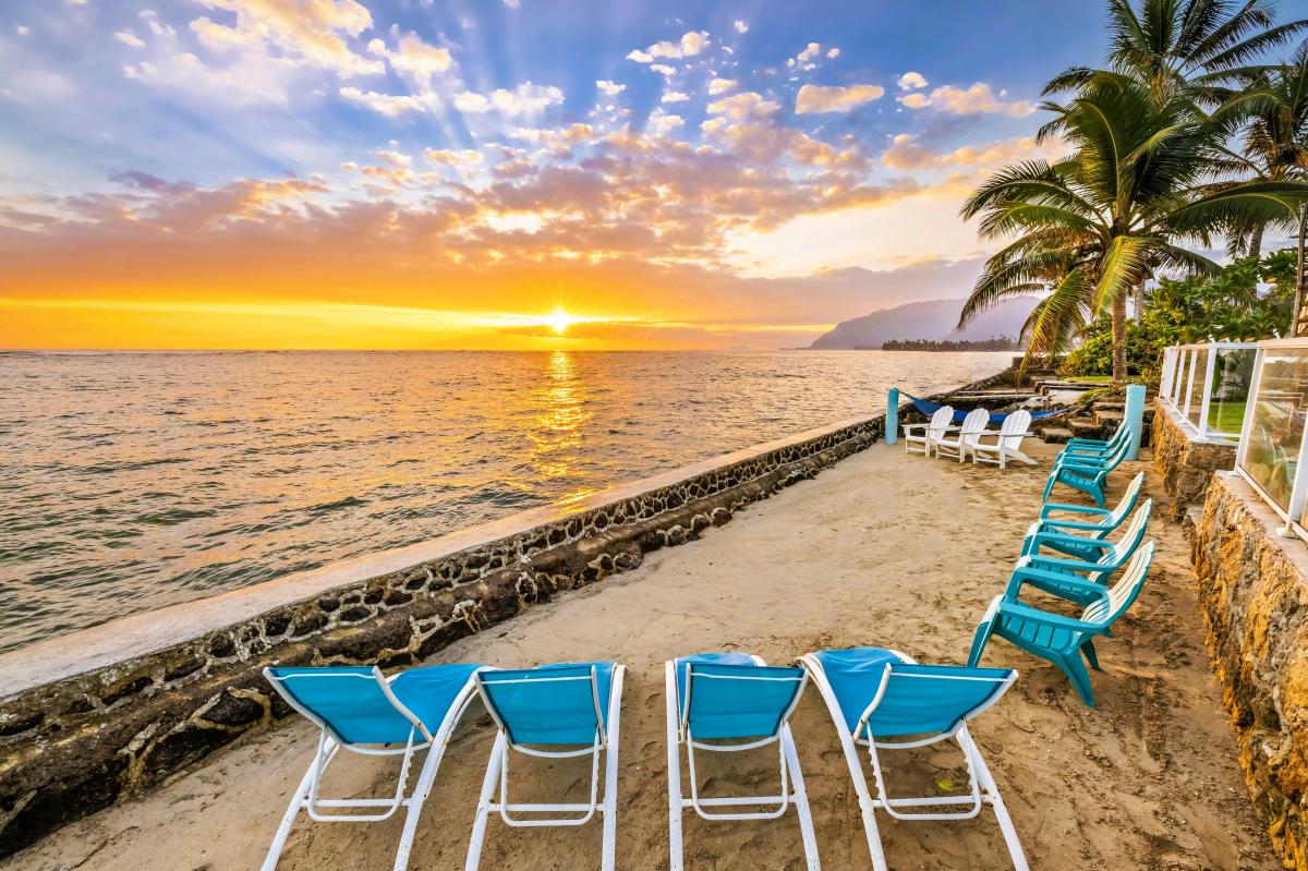 The sun drops into the water while a row of chairs waits along your own stretch of sand.