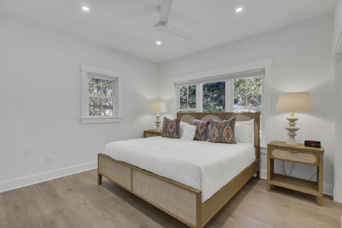 - Unwind in this airy bedroom featuring a king bed with woven frame and bold pillows - Natural light floods in through large windows for a refreshing start each morning - Dual nightstands with warm lighting create the perfect evening ambiance