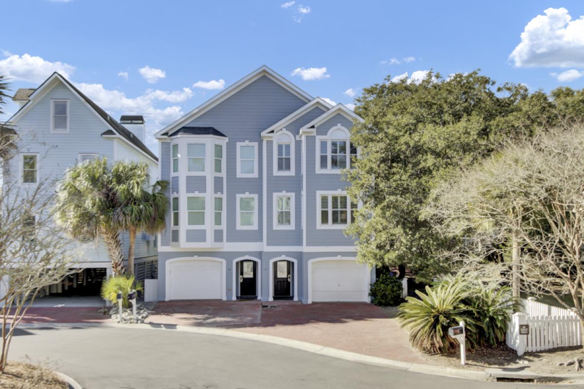 Charming coastal home with elegant gray siding and white trim nestled among mature trees and tropical landscaping.