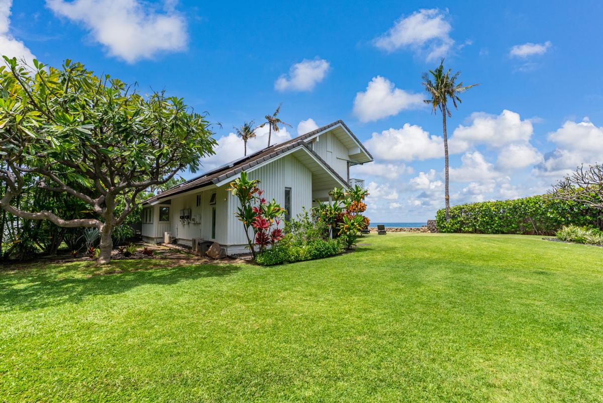 Cozy oceanfront cottage with lush tropical gardens and palm trees under endless blue skies.