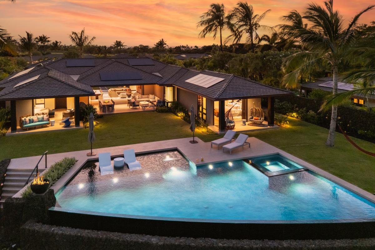 Luxury tropical estate featuring a stunning pool and hot tub, surrounded by swaying palms beneath a vibrant sunset sky.