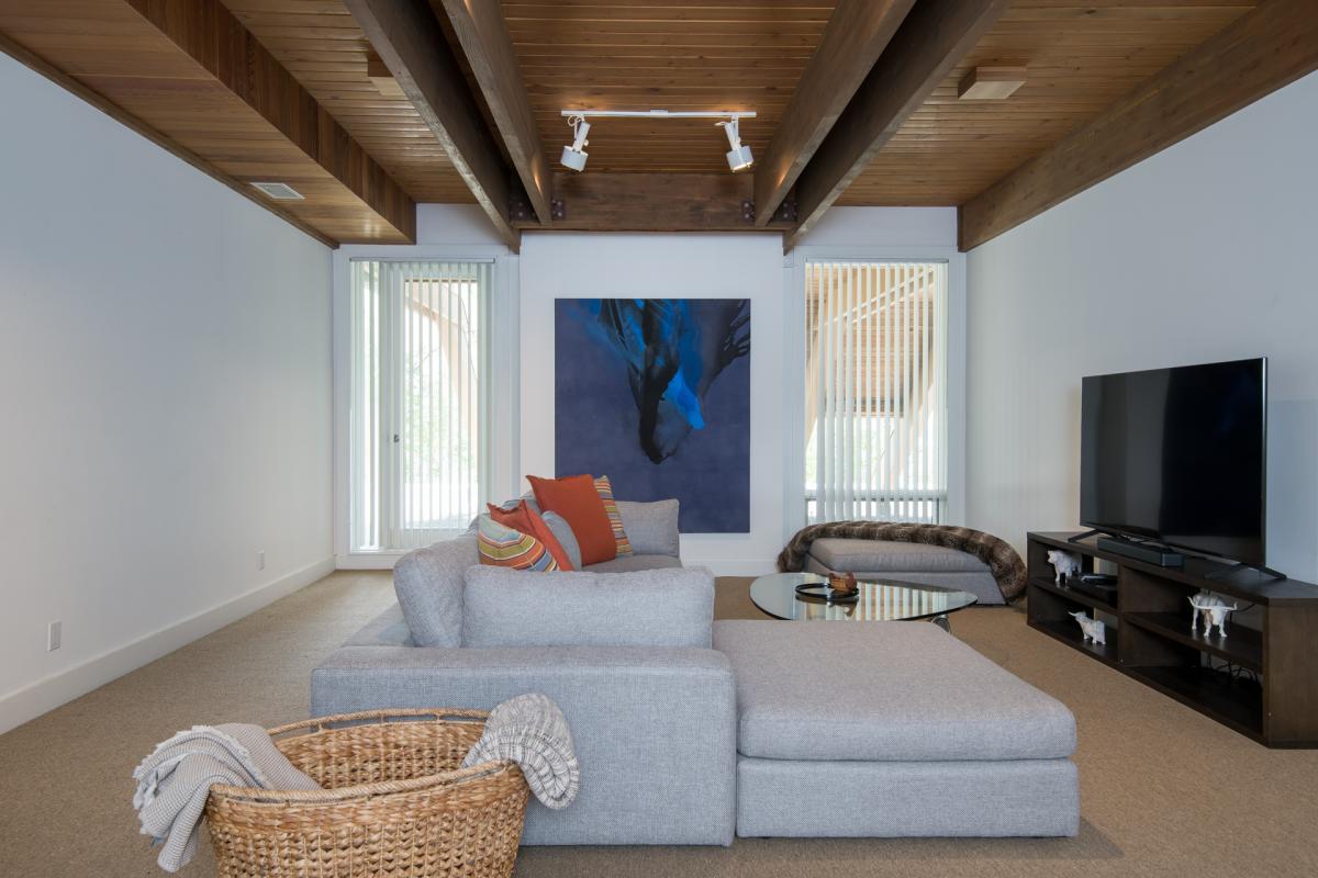 Unwind in this serene living space, where natural light filters through tall windows, highlighting warm wood beams overhead. Sink into the cozy sectional and let your worries drift away.