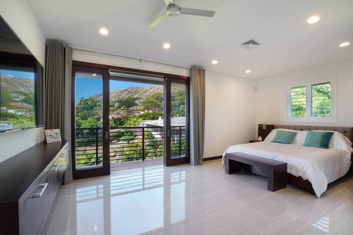 Beside the bed, glass doors give onto a lanai and the green hillside past it.