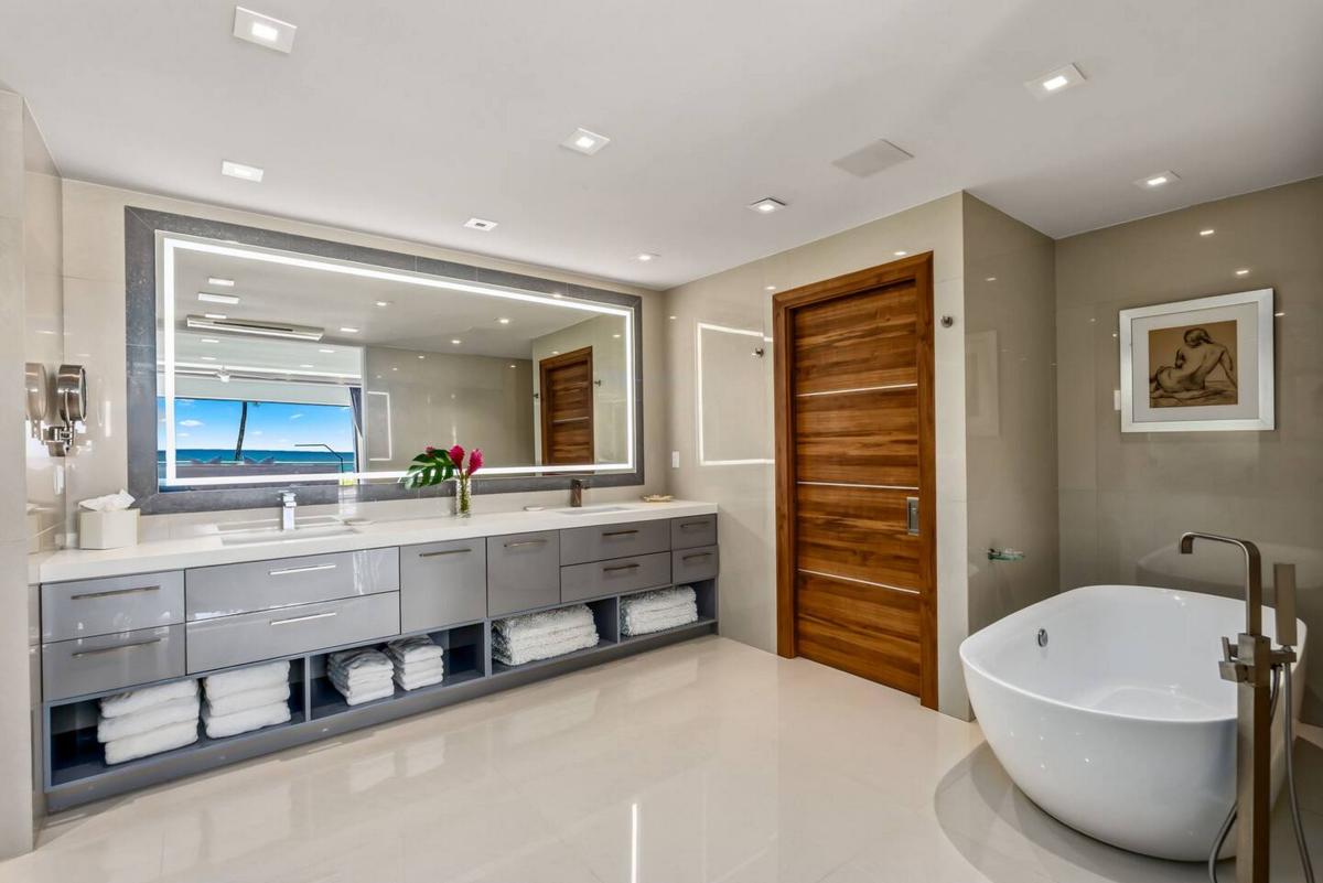 A freestanding soaking tub by the window, framed in palms and light.