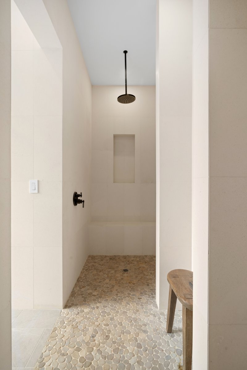 A walk-in shower finished in warm stone tile, quiet and clean-lined.