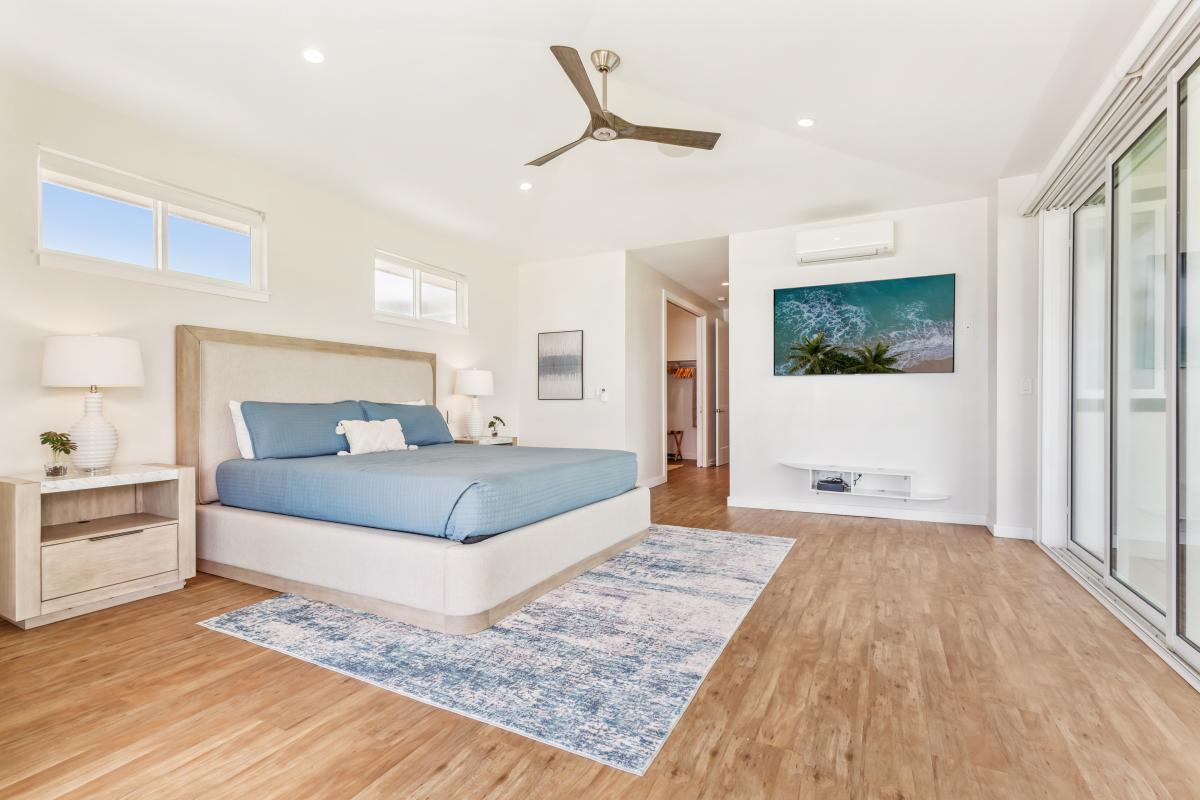 Sunlight from the lanai illuminates the space past the king bed in the primary bedroom towards the roomy closet and expansive spa-like en suite bathroom