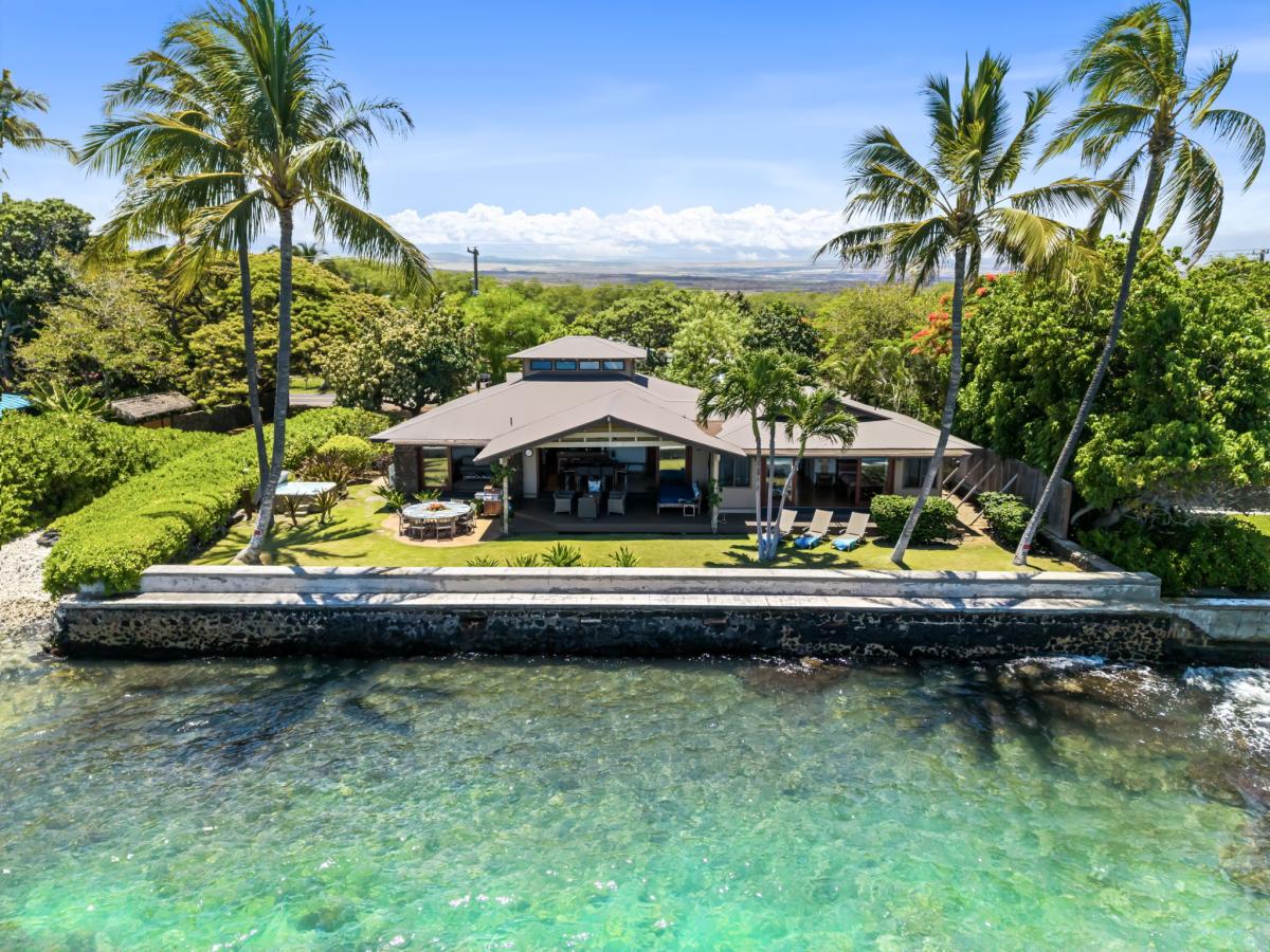 Turquoise reef water wraps the seawall, the lawn running right to the ocean's edge.